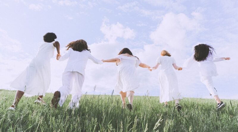 Women in white running together through a green field under a bright sky