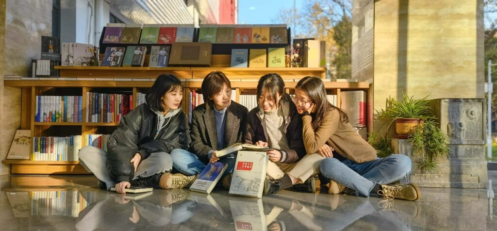 Four young women sitting outside a bookshop reading books together