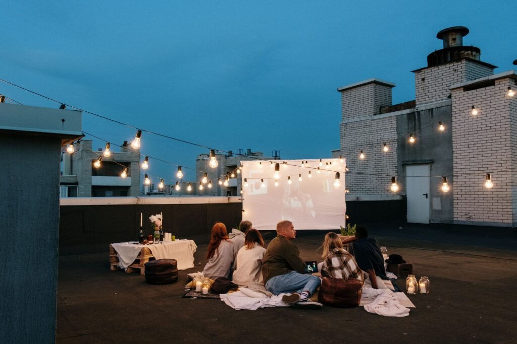 Friends watching an outdoor movie on a rooftop at dusk under string lights