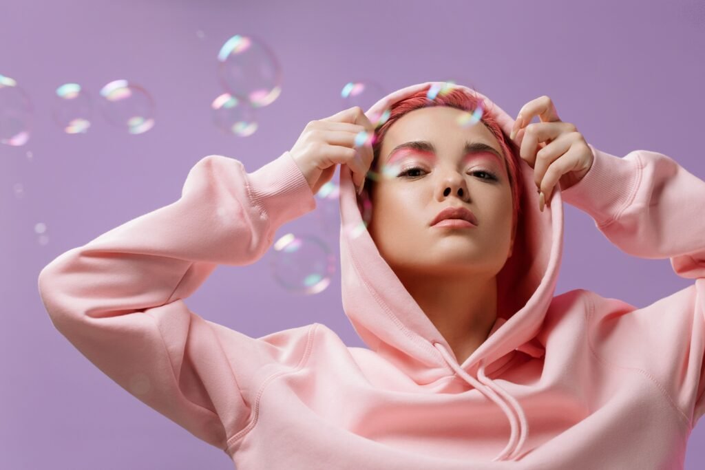 Woman in a pink hoodie with pink makeup and floating bubbles on a lilac background