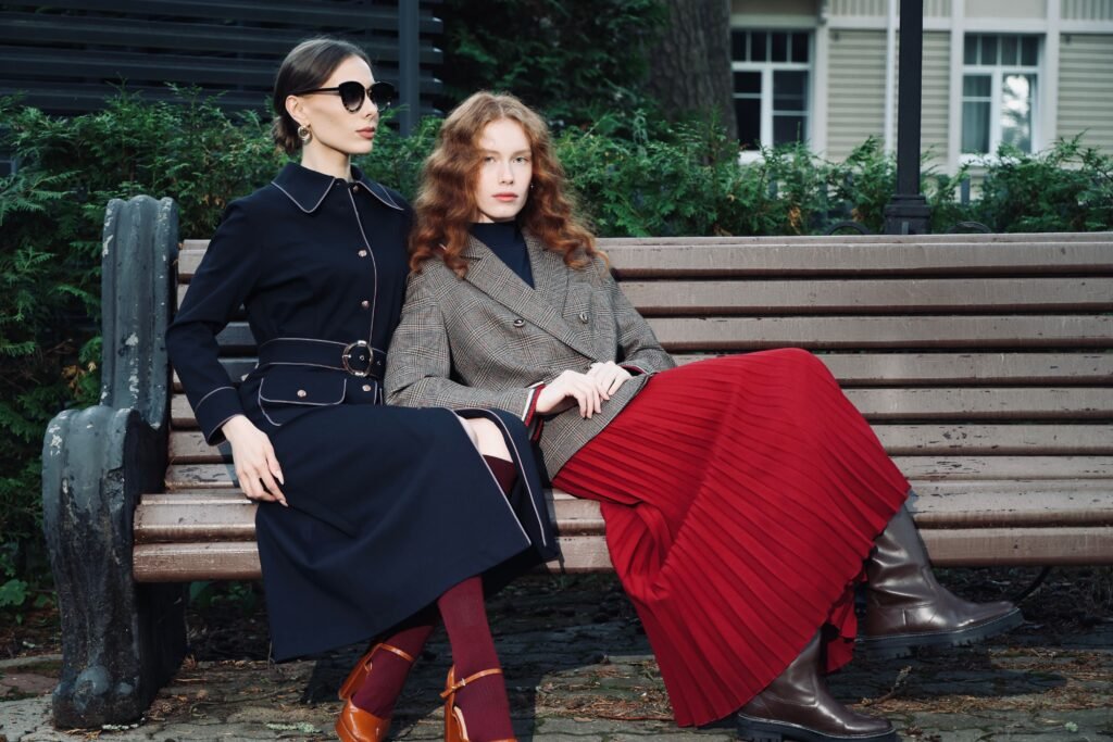 Two women in fall coats and outfits sitting on a park bench