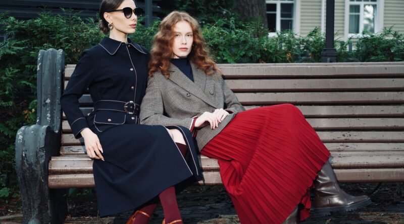 Two women in fall coats and outfits sitting on a park bench