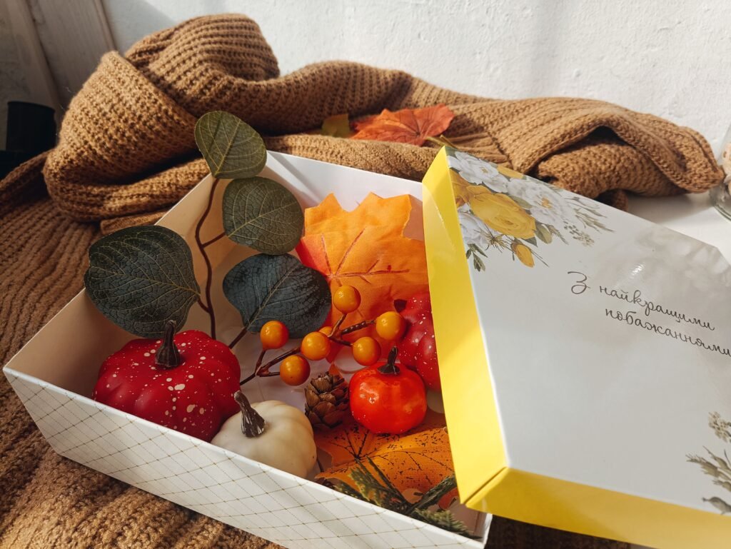 Box of small decorative pumpkins, orange berries and autumn leaves on a cozy knit sweater