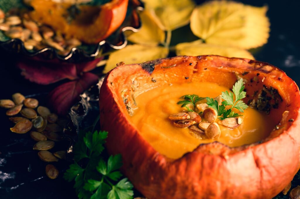 Healthy pumpkin soup served in a hollowed pumpkin with pumpkin seeds and fresh herbs