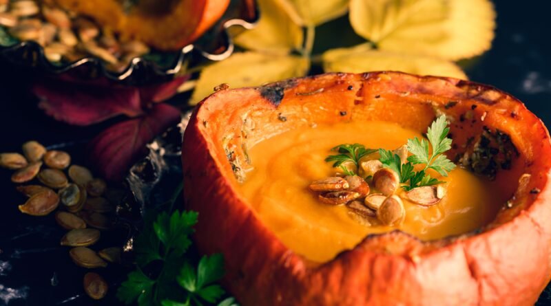 Healthy pumpkin soup served in a hollowed pumpkin with pumpkin seeds and fresh herbs