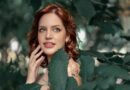 Woman with red hair and natural makeup smiling among green leaves