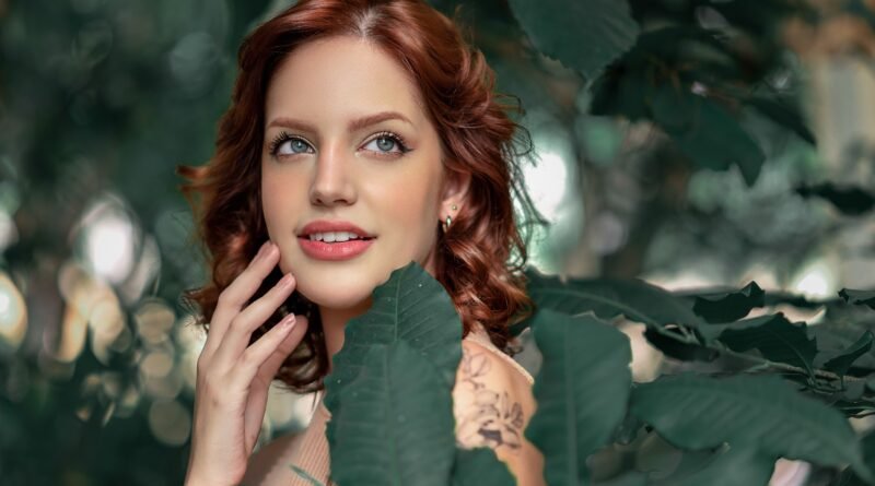 Woman with red hair and natural makeup smiling among green leaves