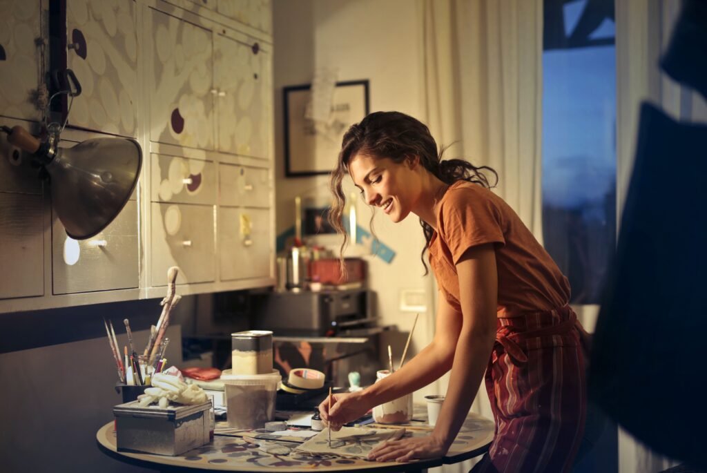 Smiling woman painting at a table at home in warm evening light