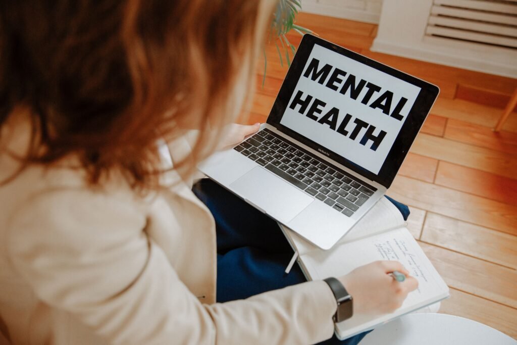 Woman writing in a notebook next to a laptop that says Mental Health