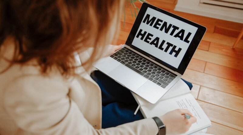 Woman writing in a notebook next to a laptop that says Mental Health
