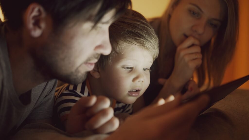 Family with a young child looking at a tablet screen in a dark room