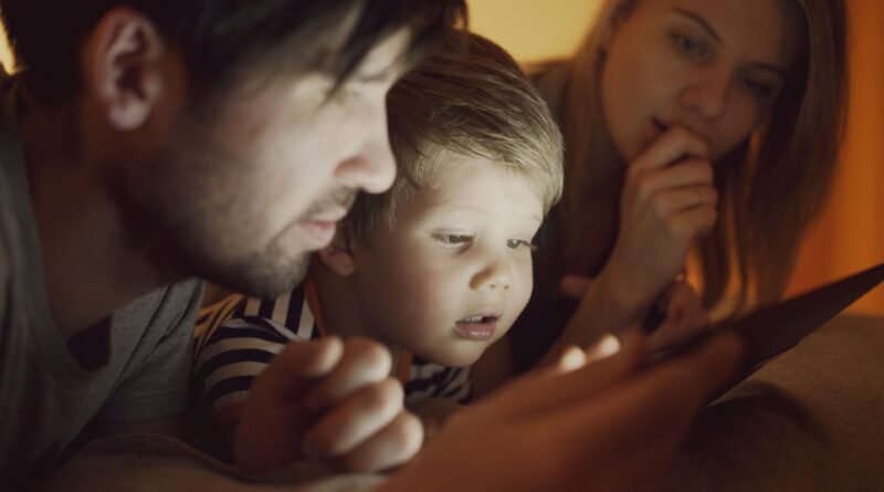 Family with a young child looking at a tablet screen in a dark room