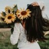 Woman with long dark hair holding a bunch of sunflowers in a field
